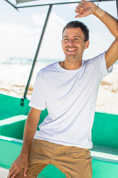 Happy white man in a white t-shirt, with an Affix Patch on his arm, standing on a beach beside a boat